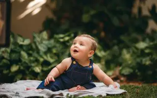 Baby in Jean Overalls Sitting on Blanket - Featured