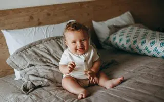 Smiling Baby Sitting on a Bed - Featured