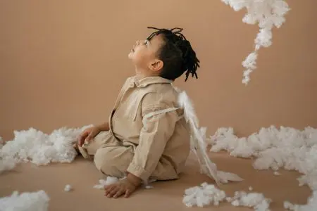 Cute black boy in angel costume near decorative clouds - Featured