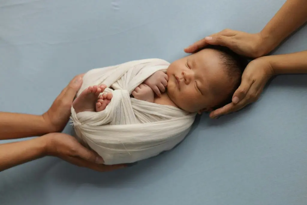 250+ Short and Sweet Three Letter Boy Names 7 A newborn wrapped in a blue blanket is being held by two hands