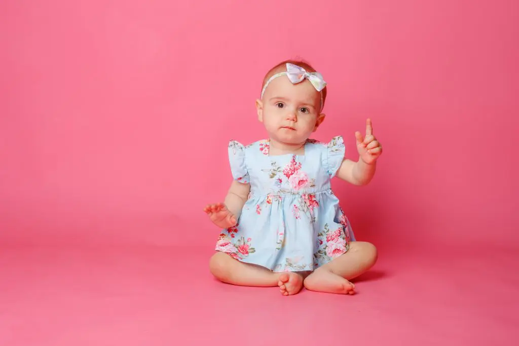 baby girl dressed in a dress sitting on a pink background