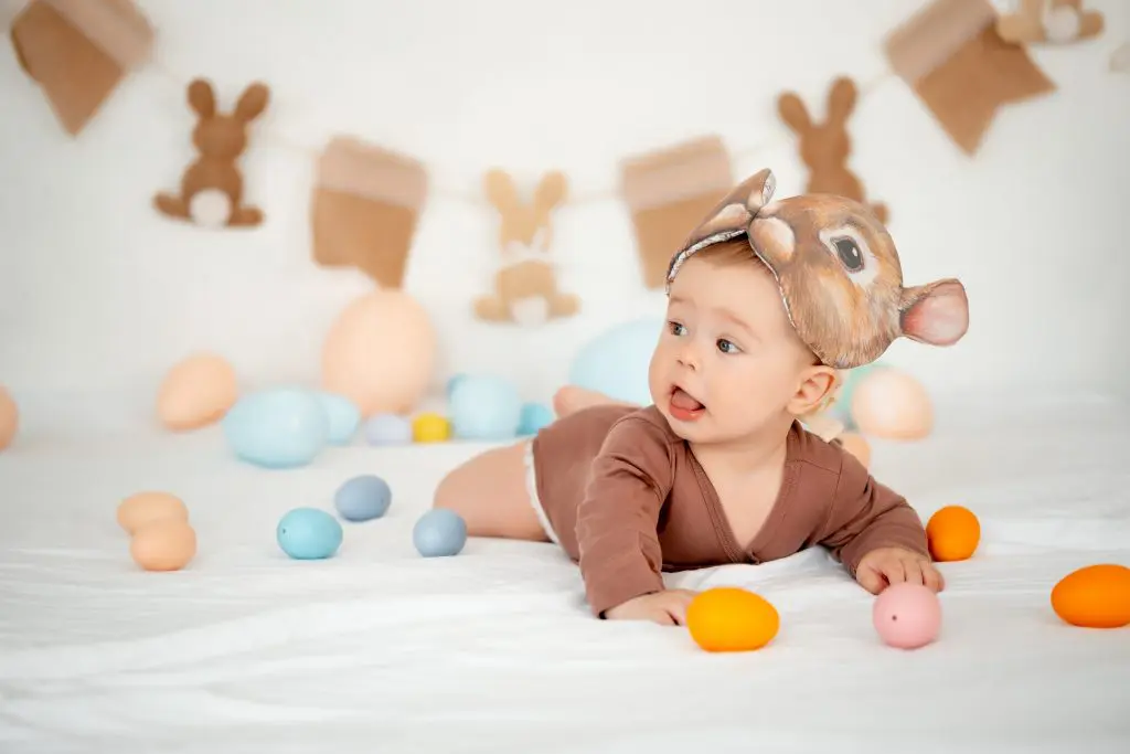 A baby lies among Easter colorful eggs with a rabbit mask on his head