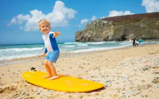 Cute blond toddler boy practice surfboard posing