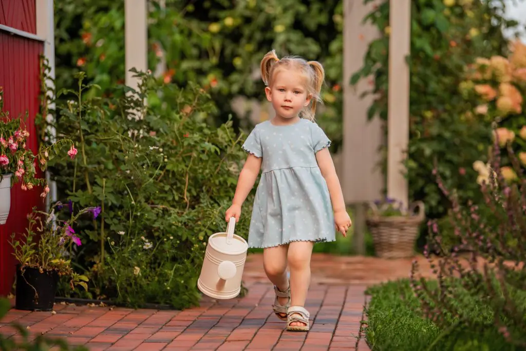 little girl in a blue dress walks along a garden path