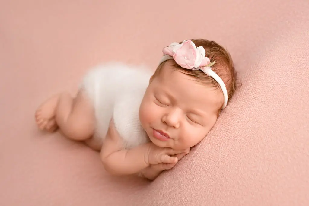 Newborn baby girl sleeping in a white jumpsuit