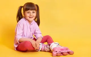 Dark haired laughing girl with two ponytails sitting in roller skate on floor