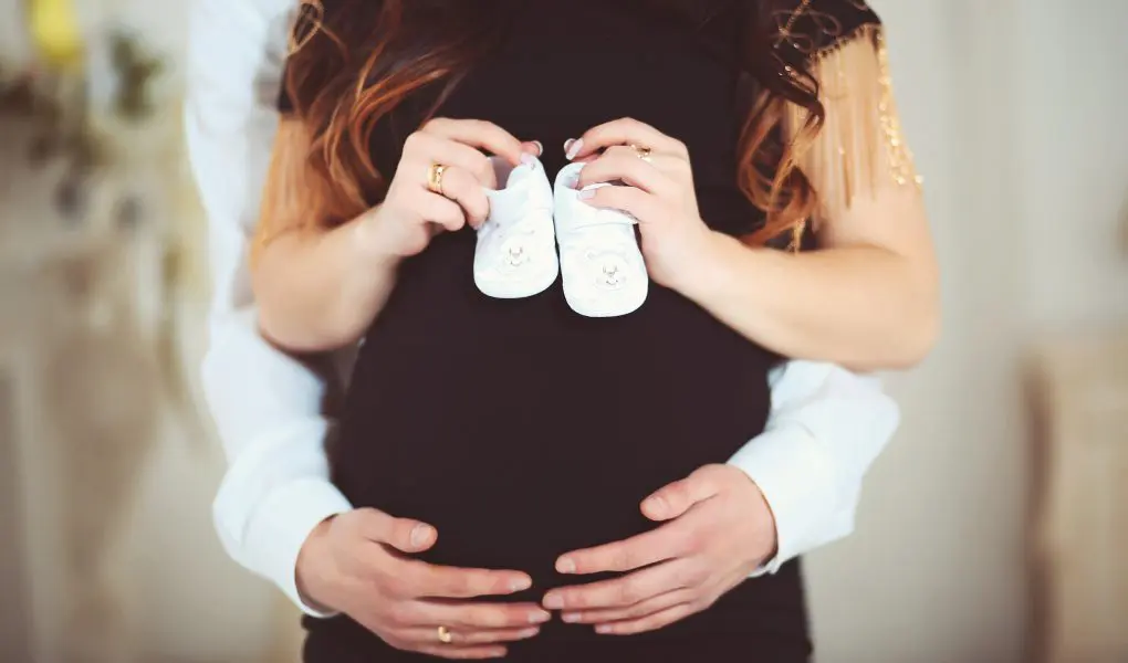 Pregnant woman holding baby shoes and of her husband at home