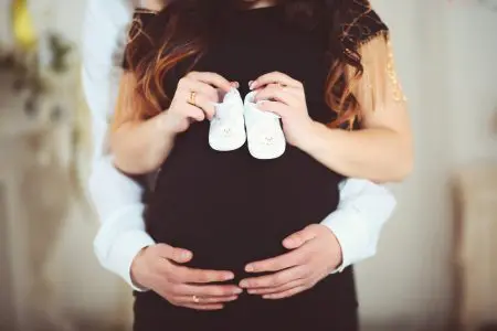 30 Unique Pregnancy Reveal Ideas for Social Media 3 Pregnant woman holding baby shoes and of her husband at home