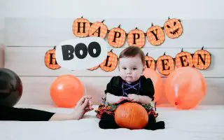 Cute girl with pumpkin sitting on bed at home
