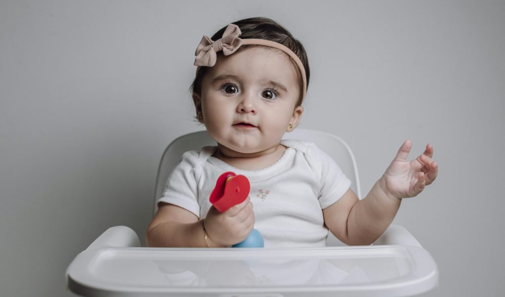 182 Modern Girl Names That Are Perfectly On-Trend 1 Baby Girl Sitting on a Feeding Chair with a Toy