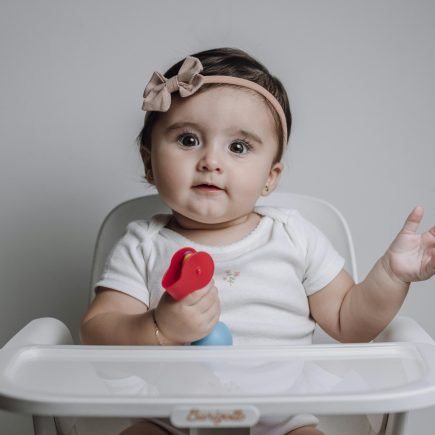 Baby Girl Sitting on a Feeding Chair with a Toy