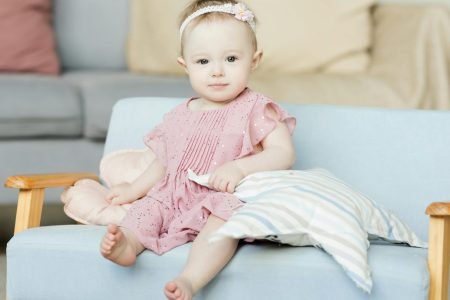 Baby Girl in Pink Dress Sitting on Sofa - Featured