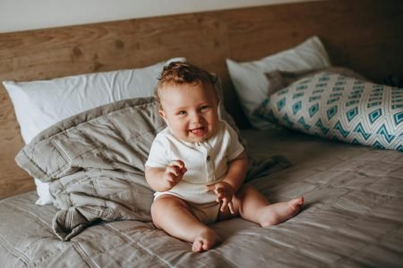 Smiling Baby Sitting on a Bed - Featured