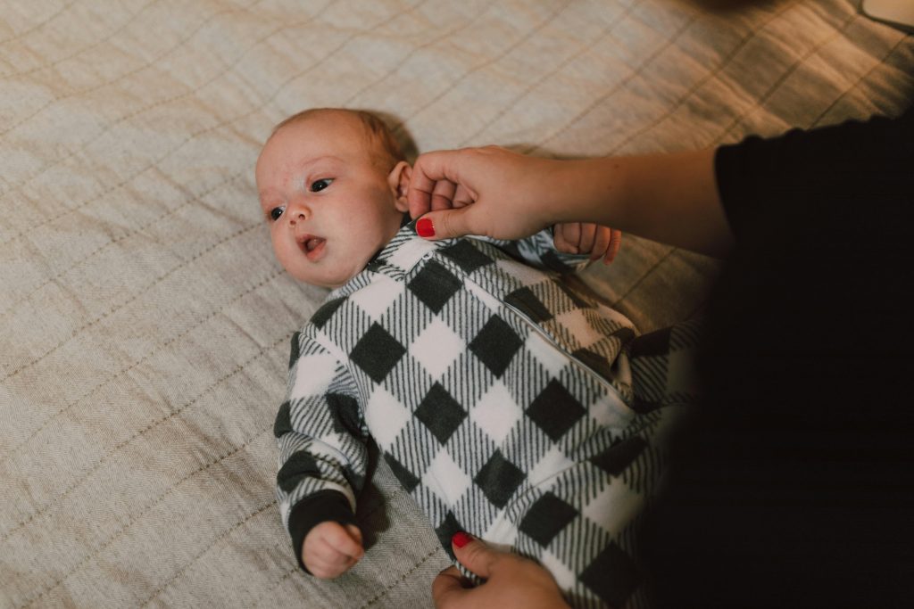 Baby in Gray and White Checkered Onesie Lying on Bed