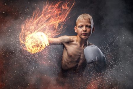 Young boy wearing boxing gloves shows a boxing hook.