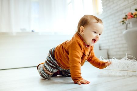 Happy child in orange sweater playing on the floor