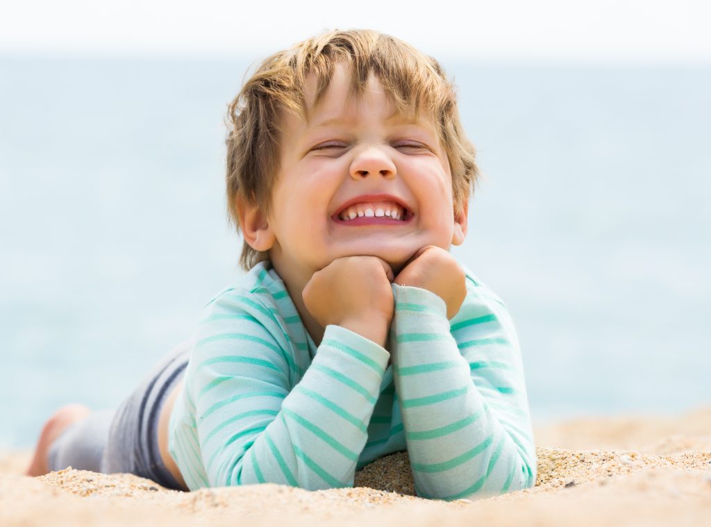 Happy laughing baby girl laying on sand beach