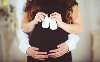 Pregnant woman holding baby shoes and of her husband at home