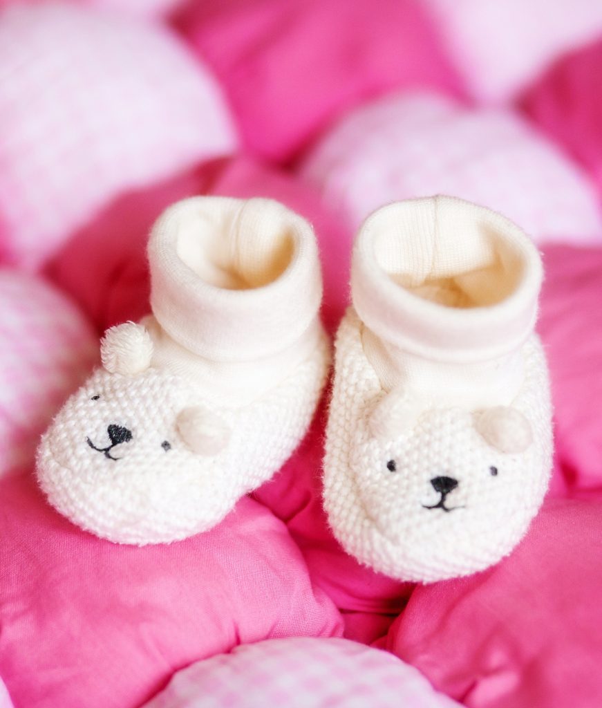 Cute white baby booties on pink blanket. Pregnancy concept
